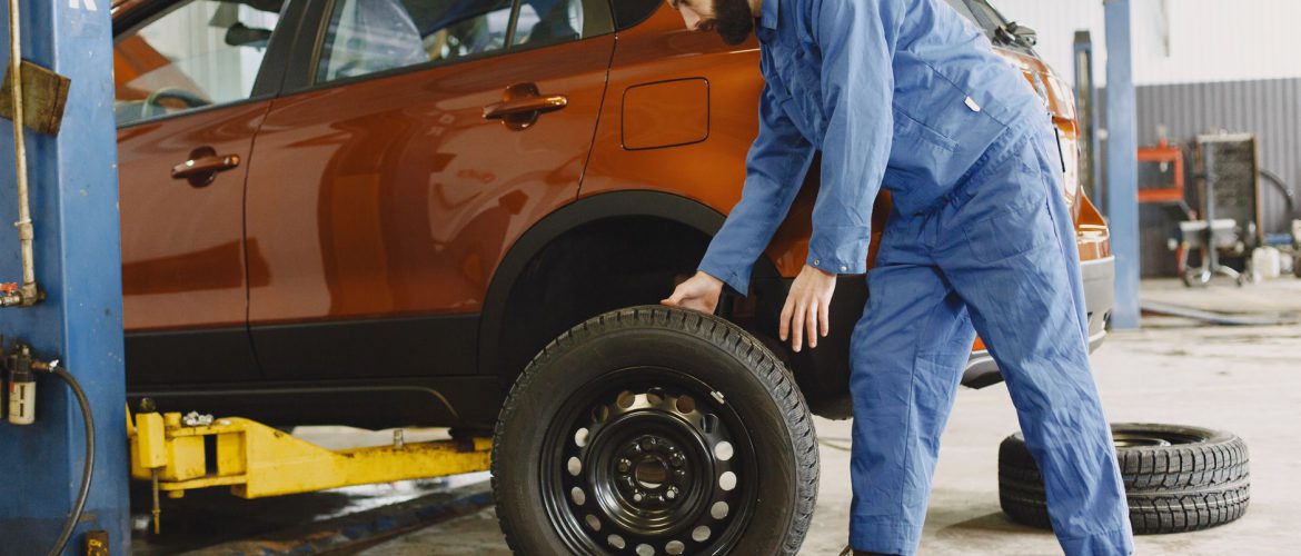Mechanic in blue coveralls replacing tire on red SUV in repair shop garage.
