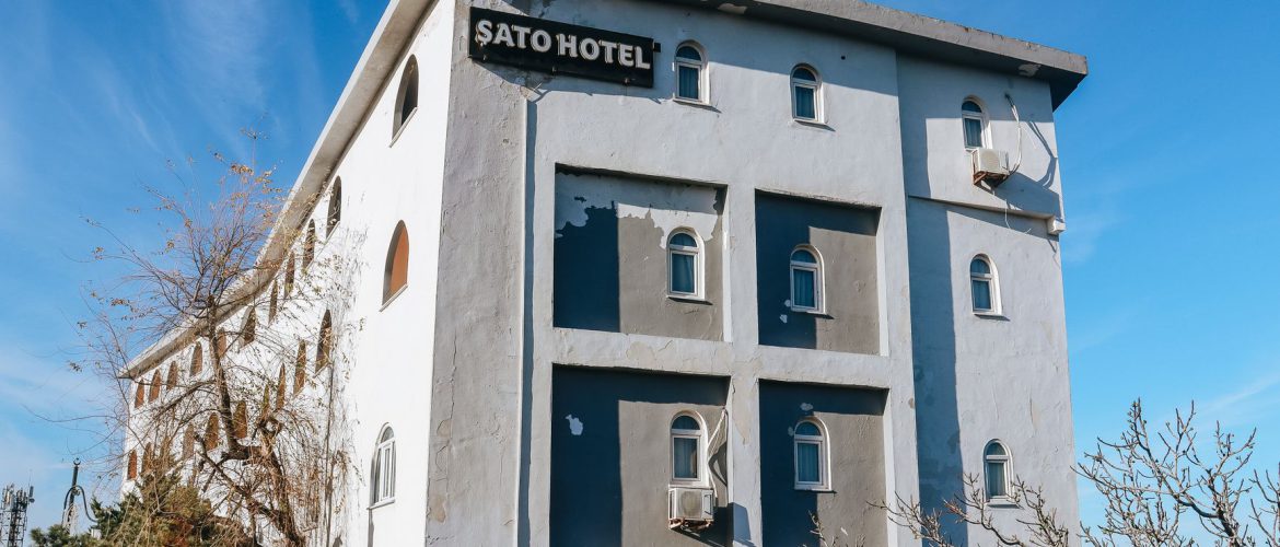 Parlak mavi gökyüzünün altında dökülen boyasıyla Sato Otel binası, kentsel mimariyi sergiliyor.